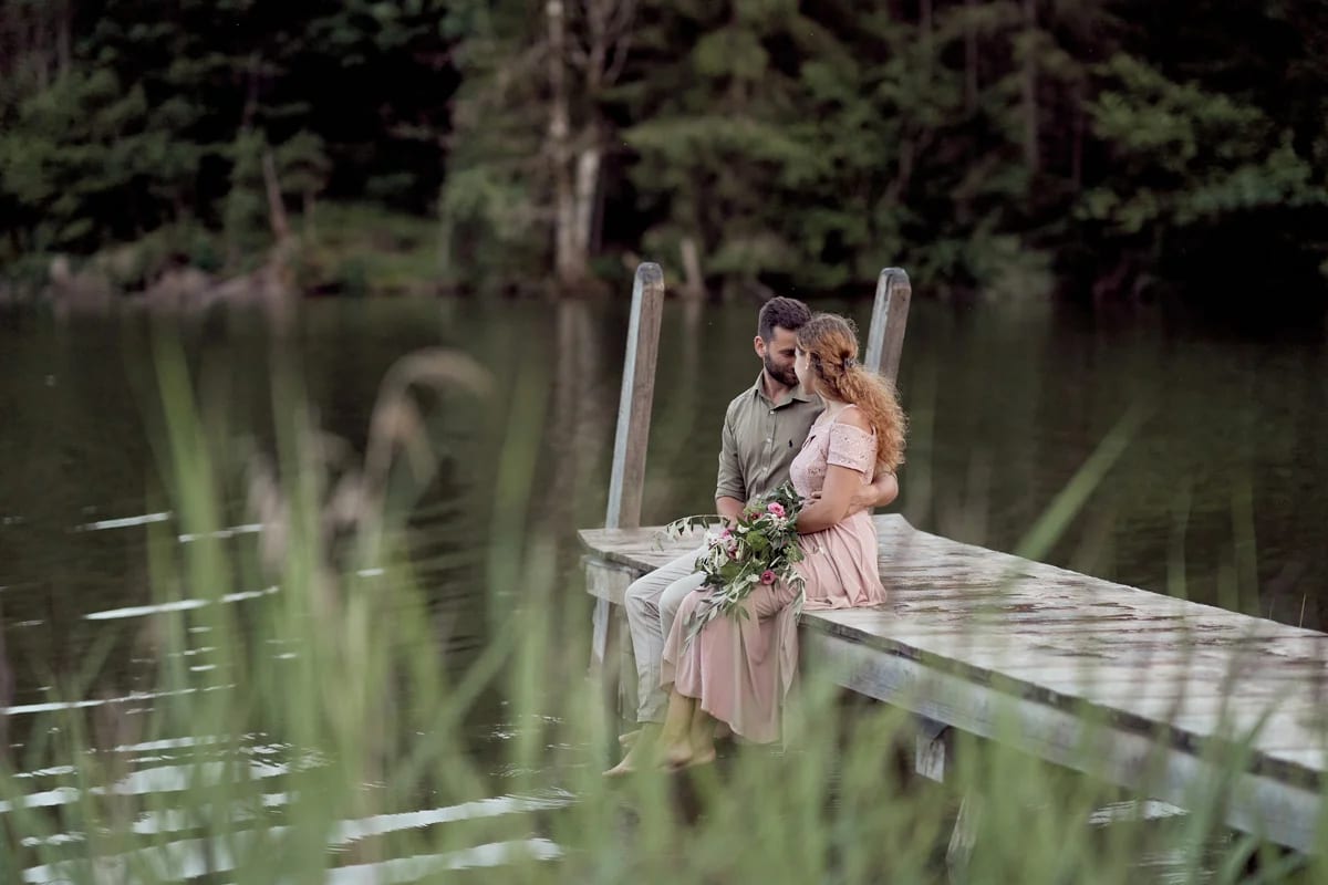 Romantic couple portrait on the wooden jetty of Lake Geroldsee with a mountain reflection