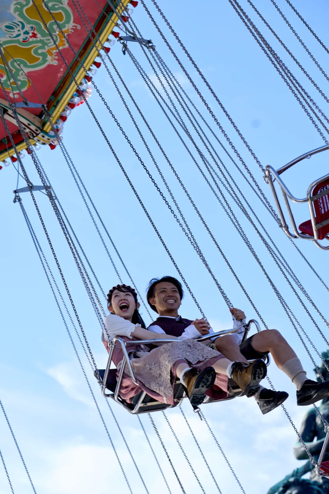 Engaged couple in Tracht swinging together on the chain carousel at Oktoberfest in Munich