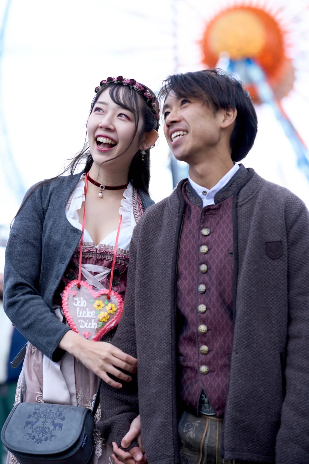 Engaged couple in Tracht laughing hand in hand on the chain carousel during their engagement photoshoot at the Wiesn in Munich